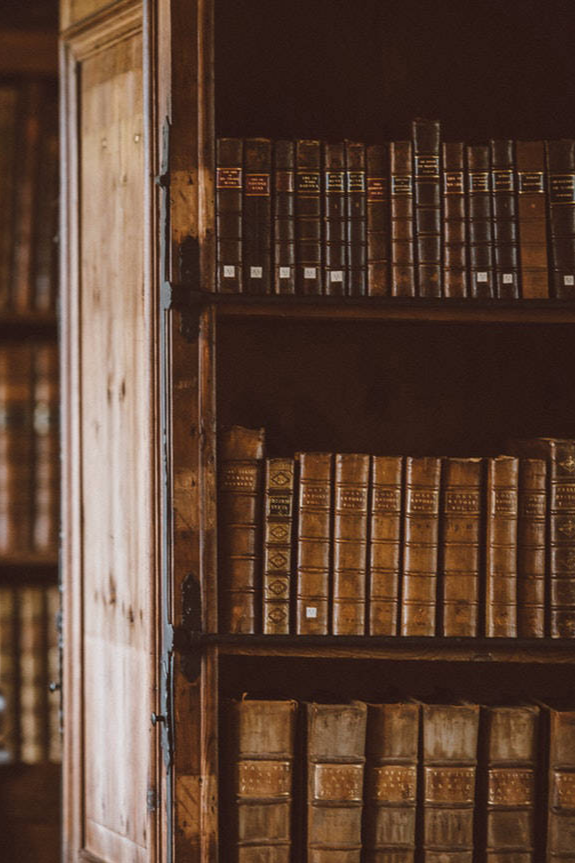 Rows of antique leather-bound books on a dark wooden bookshelf in a library